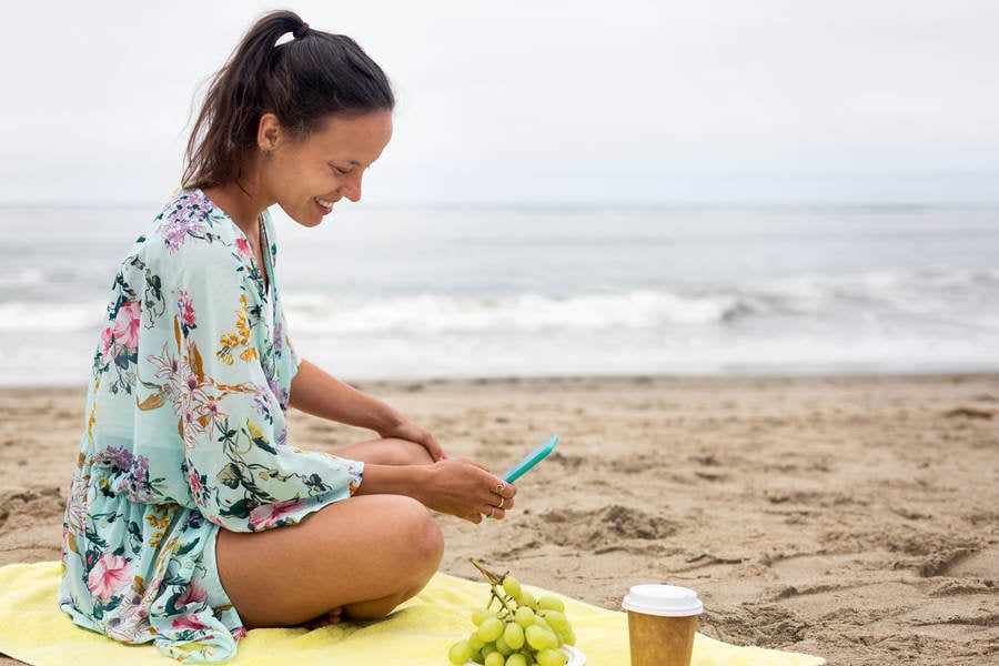 Young Smiling Woman with a Smartphone Sitting on a Beach Towel