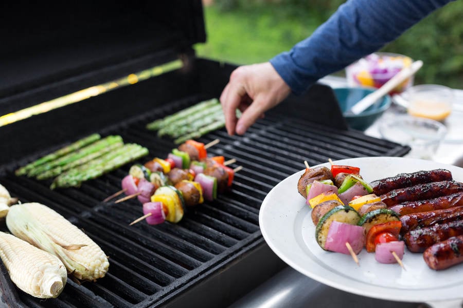 Man Grilling Vegetable Skewers and Sausages on a Barbecue