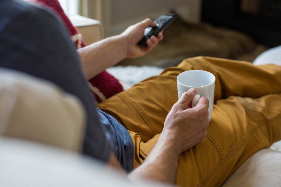Man Holding a Coffee Cup and Using a TV Remote Control