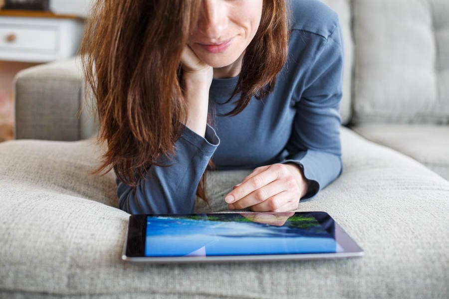 Low-Angle View of a Woman Relaxing on a Sofa Looking at a Digital Tablet