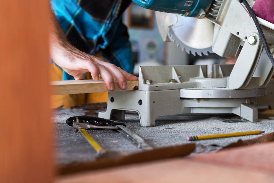Handyman Cutting a Wooden Board with a Miter Saw in a Workshop