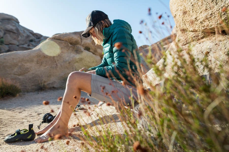 Woman Sitting on a Rock and Putting on Climbing Shoes
