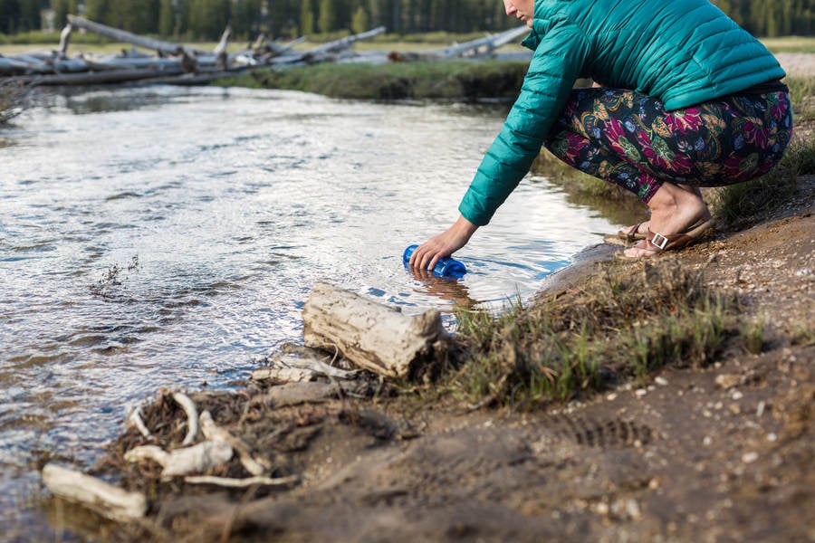 Woman Filling a Bottle with Pure Water from an Alpine Creek