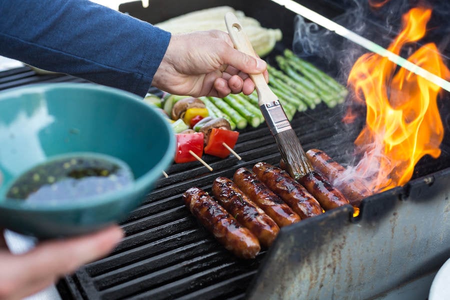 Man Braising Sausages on a Barbecue Grill with a Marinade