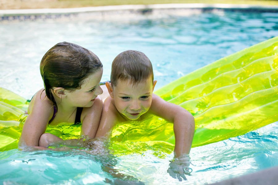 Two Children Floating on an Inflatable Air Mattress in a Swimming Pool
