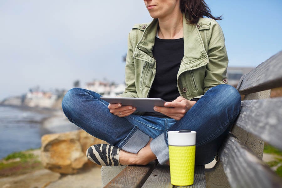 Woman Sitting on a Bench on a Coast Holding a Digital Tablet
