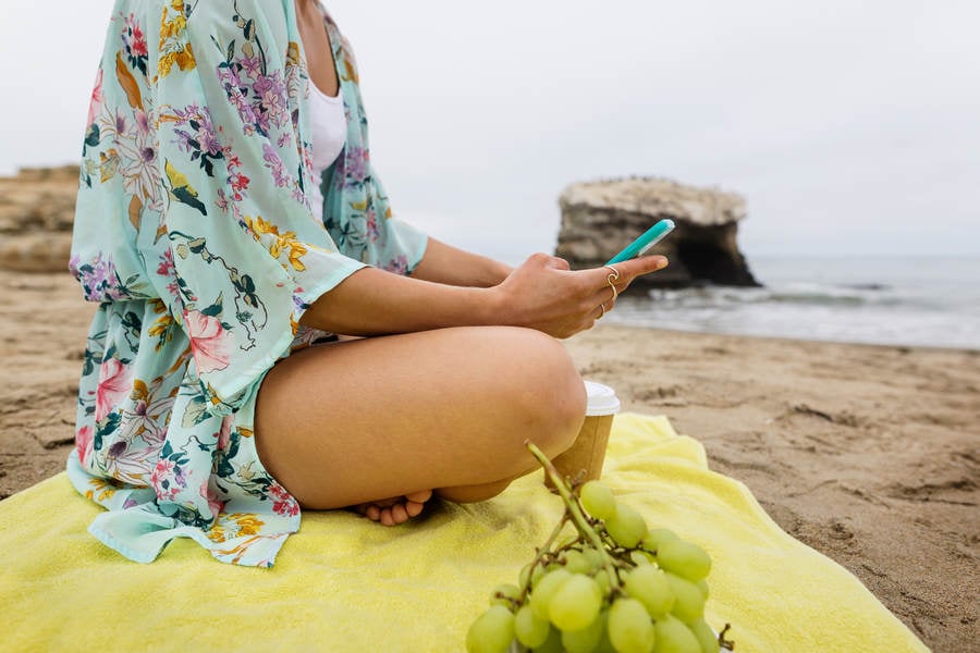 Young Woman Sitting on a Beach Towel and Browsing on a Cell Phone
