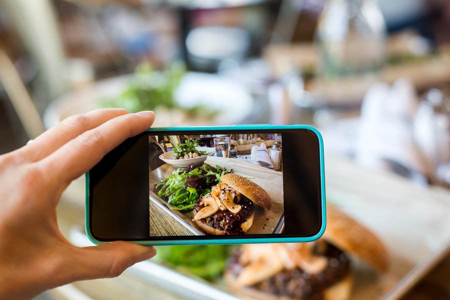 Woman's Hand Holding a Smartphone and Taking Picture of Her Meal