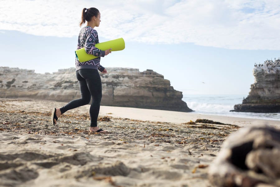 Young Athletic Woman with a Yoga Mat Walking on a Sandy Beach