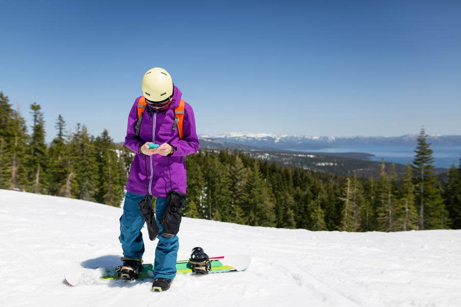 Female Snowboarder Using a Cell Phone on a Top of a Ski Run