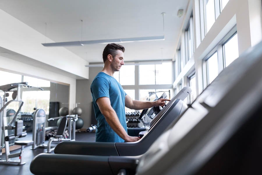 Man Selecting a Workout Setting on a Treadmill in a Gym