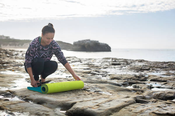 Smiling Athletic Woman Rolling a Yoga Mat on a Rocky Beach