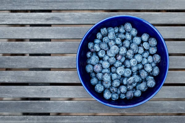 Overhead View of a Bowl Full of Blueberries on a Slotted Table