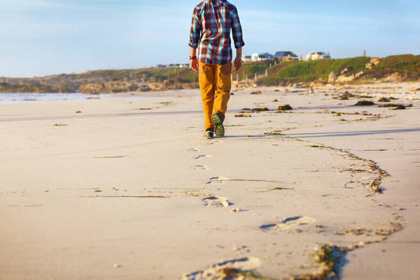 Low-Angle View of a Man Walking on the Beach Leaving Footprints Behind