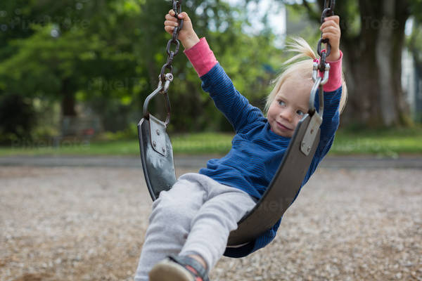 View of a Toddler Girl Sitting on a Swing at Playground