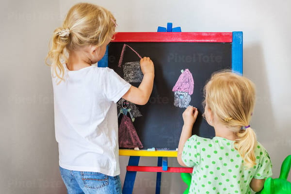Young Twin Sisters Drawing on a Chalkboard at Home