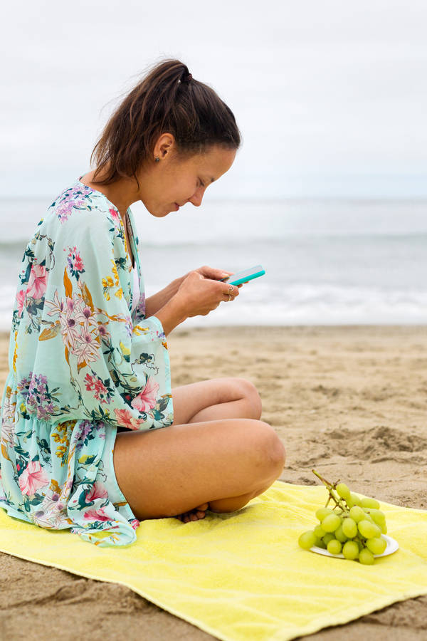 Young Woman Sitting on a Beach and Browsing on a Cell Phone