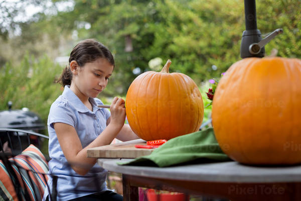 Focused Young Girl Drawing on a Pumpkin Before Carving