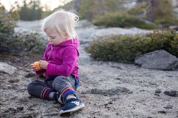 Toddler Girl Sitting on the Ground and Peeling Tangerine