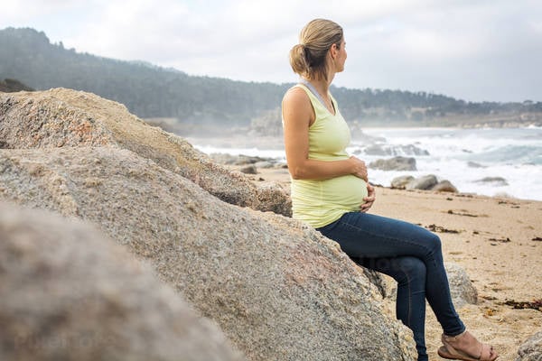 Pregnant Woman Sitting on a Rock on a Beach