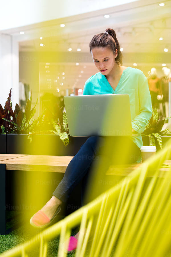 Woman Sitting on a Bench in a Shopping Mall and Working on a Laptop