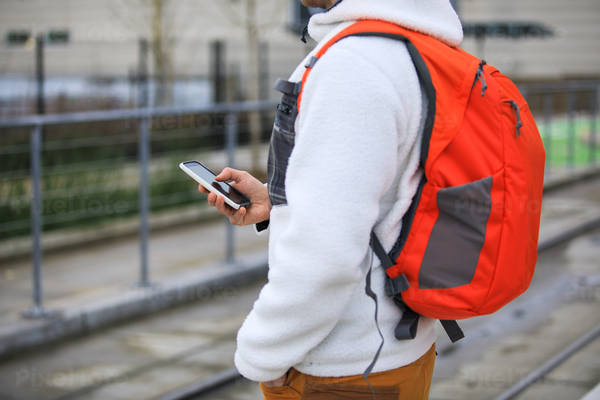 Man with a Backpack Standing on a Train Platform and Scrolling Through His Phone