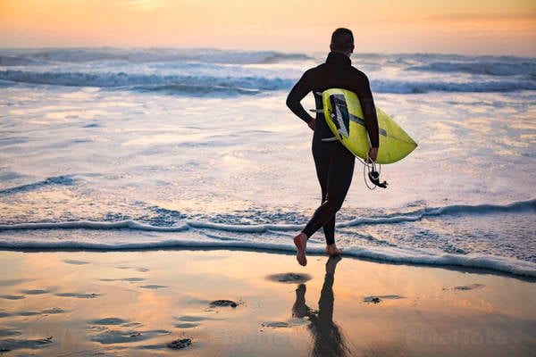 Male Surfer with a Surfboard Running on a Beach During Sunset