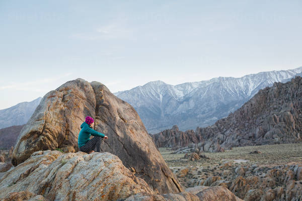 Woman in a Beanie Sitting on a Rock and Looking at Mountains