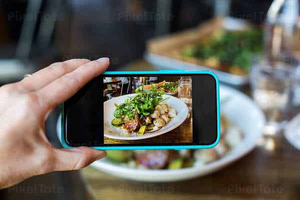 Woman's Hand Holding a Cell Phone and Taking Picture of Her Meal