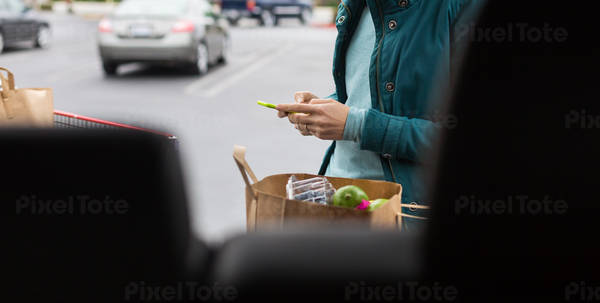 Woman Typing on a Cell Phone and Standing by a Car and a Shopping Cart
