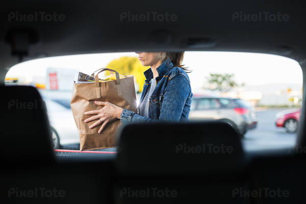 Woman Loading Bag with Groceries in a Trunk of a Hatchback Car