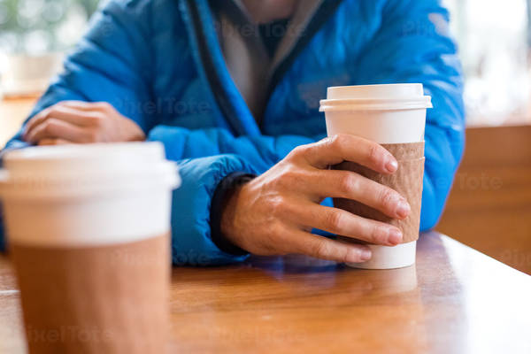 Table-Level View of a Man in a Down Jacket Holding a Cup of Coffee in One Hand