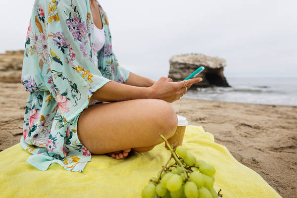 Young Woman Sitting on a Beach Towel and Browsing on a Cell Phone