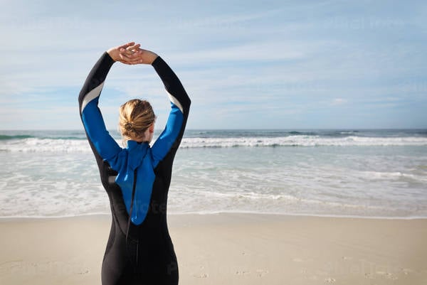 Young Woman in a Wetsuit Stretching on a Beach