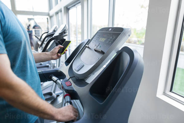 Man with a Cell Phone Standing on a Treadmill in a Gym