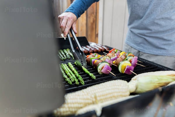 Man Grilling Vegetables and Sausages on a Barbecue