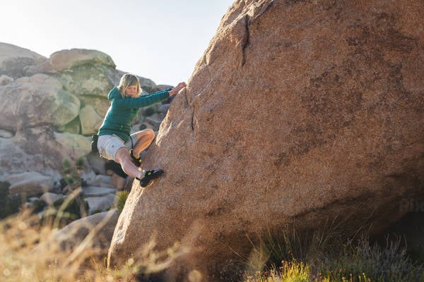 Young Woman in a Down Jacket Bouldering on a Granite Slab