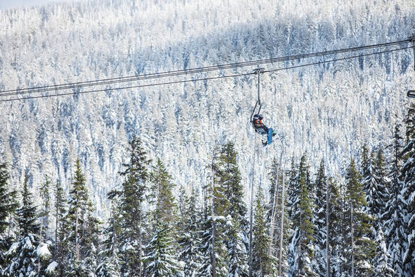 Snowboarders on a Chairlift with Snow-Covered Trees in the Background