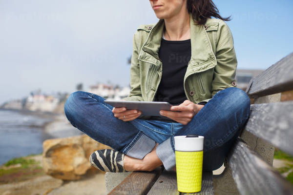 Woman Sitting on a Bench on a Coast Holding a Digital Tablet
