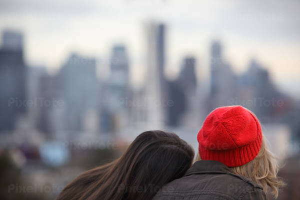 A Girl Leaning on Other Girl's Shoulder in a Park with a View of the City