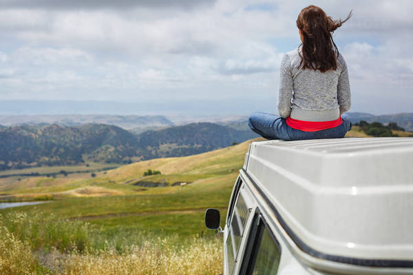 Girl Sitting on the Roof of a VW Bus Looking at Rolling Hills in the Distance