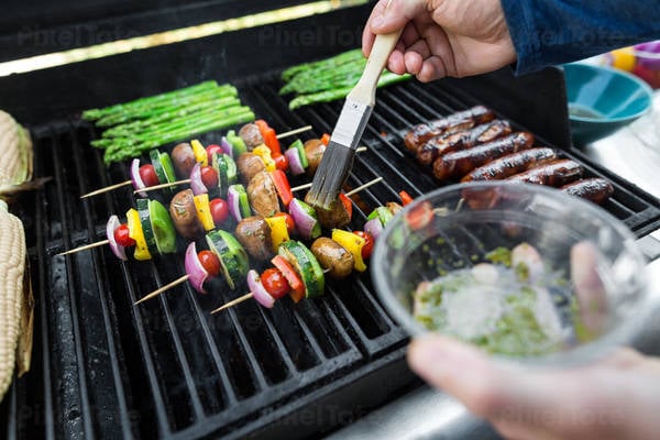 Man braising vegetable skewers on a BBQ grill with a brush