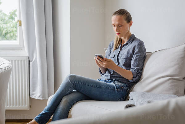Young Woman Sitting on a Couch and Using a Smartphone