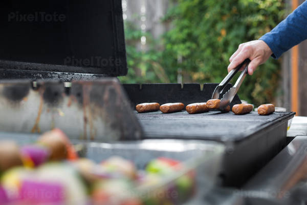 Man Placing Sausages on a Barbecue in a Garden