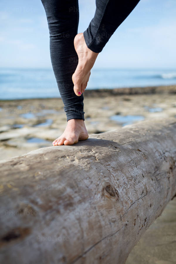 Woman Practicing a Yoga Tree Pose on a Log on a Beach
