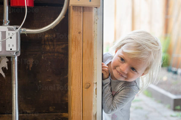 Cute Toddler Girl Peeking from behind the Door Frame in a Garage  