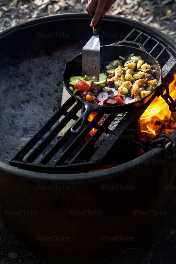 Man Using Metal Spatula to Cook Breakfast on an Outdoor Fire Pit