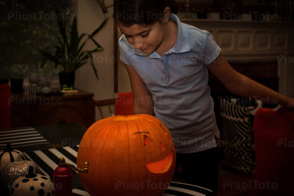 Girl Looking Inside an Illuminated Carved Pumpkin