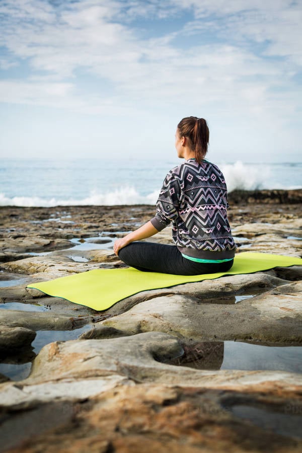 Young Athletic Woman Meditating on a Yoga Mat by the Ocean