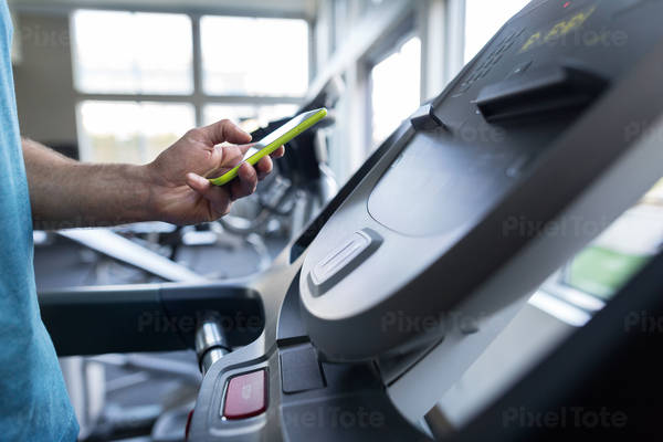 Man Standing on a Treadmill and Checking a Fitness App on a Smartphone